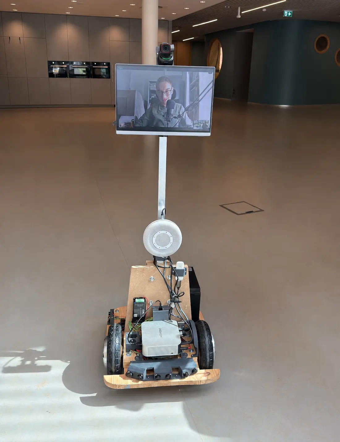 IP-Car robot in een schoolgang, met Thomas zichtbaar op het scherm terwijl hij vanuit huis op afstand de les volgt